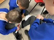 two Year 2 boys measuring the length of another boys foot with his shoe off