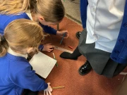 Year 2 children measuring a girls foot with a ruler who has taken off her shoe