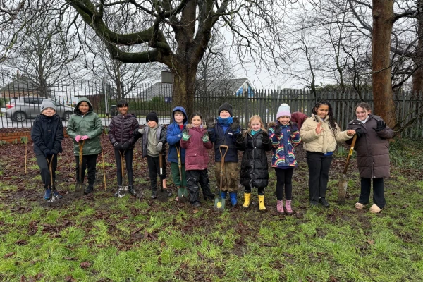 11 school children standing on a school filed holding spades and waving.